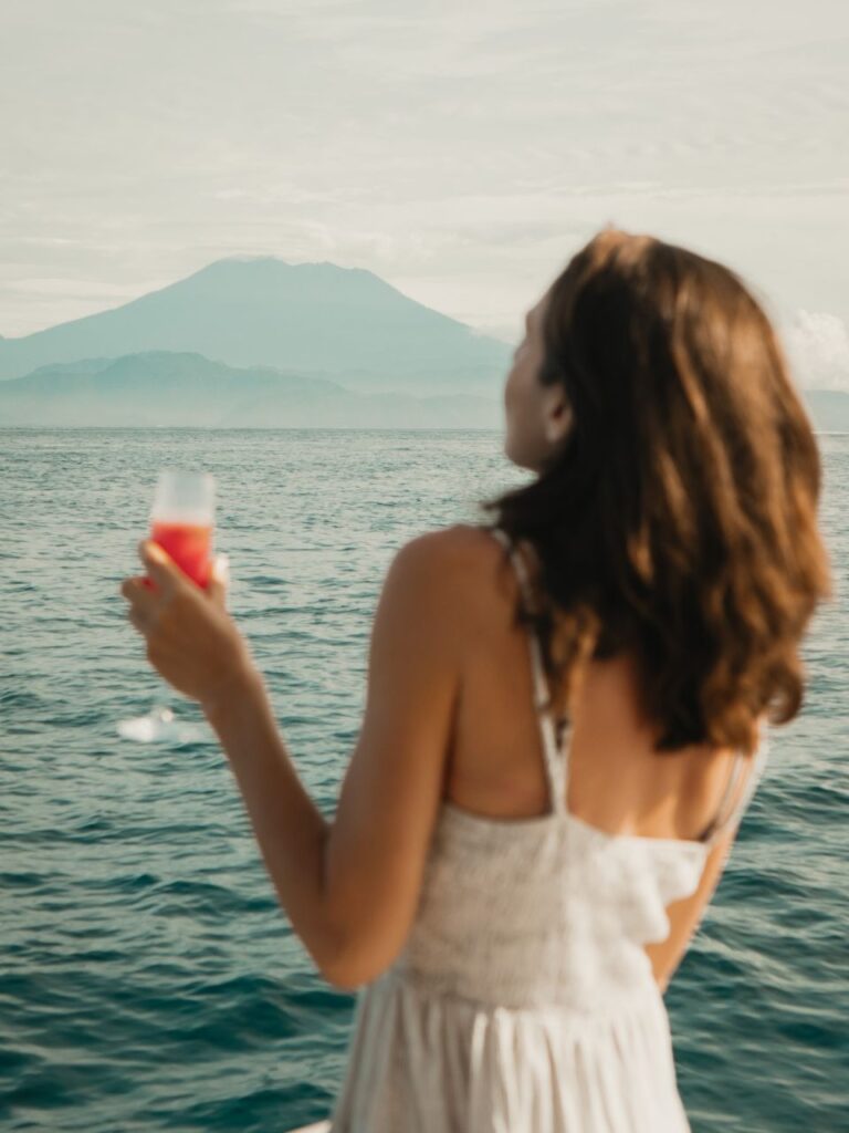 woman enjoying a drink with ocean views during a catamaran cruise with blurred Nusa Lembongan in the back ground.